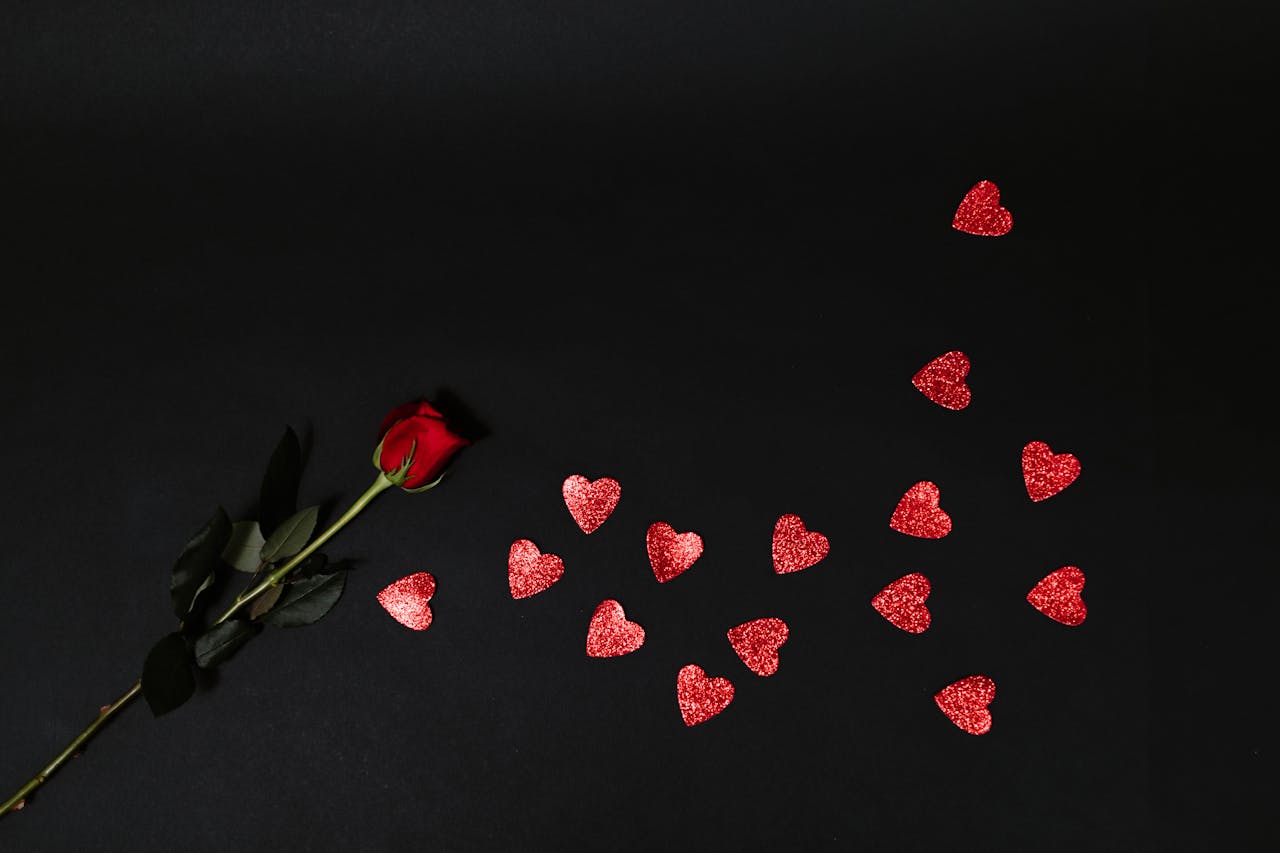services-05 A dramatic image of a single red rose with scattered heart shapes on a dark background, perfect for Valentine's themes.